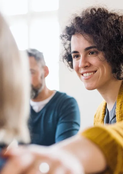 A woman with curly hair smiles warmly during a conversation in a bright room.