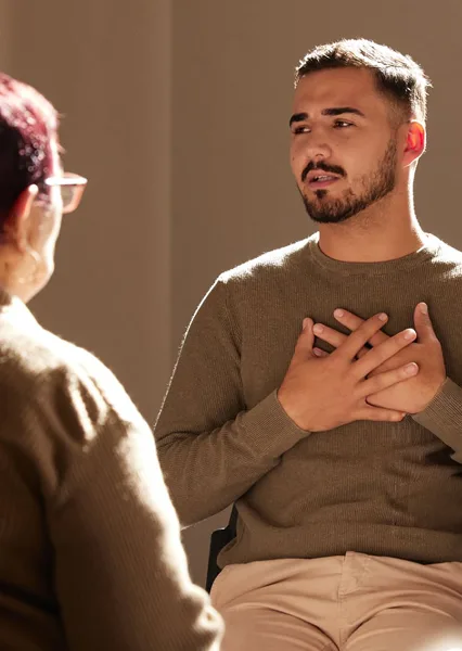 A man gestures while speaking to a woman in a cozy, sunlit setting.